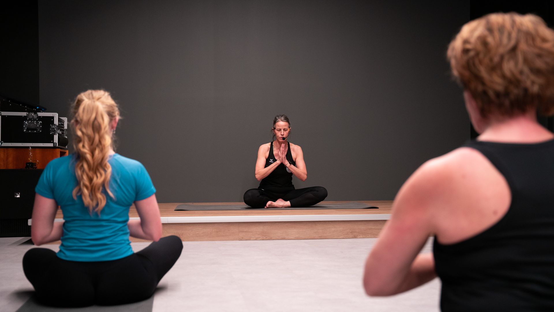 Drie mensen in een yogastudio, één in lotushouding in het midden.