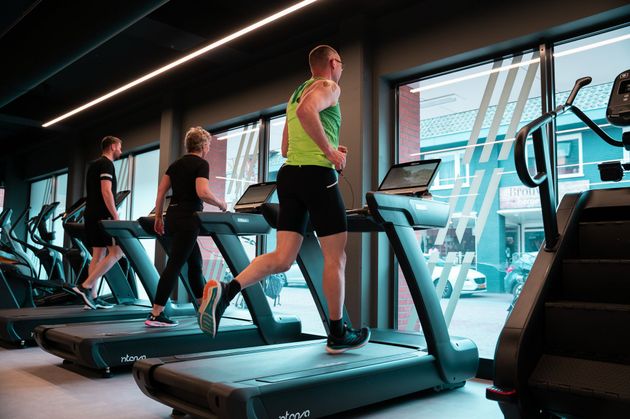 Drie mensen rennen op loopbanden in een moderne sportschool met grote ramen.