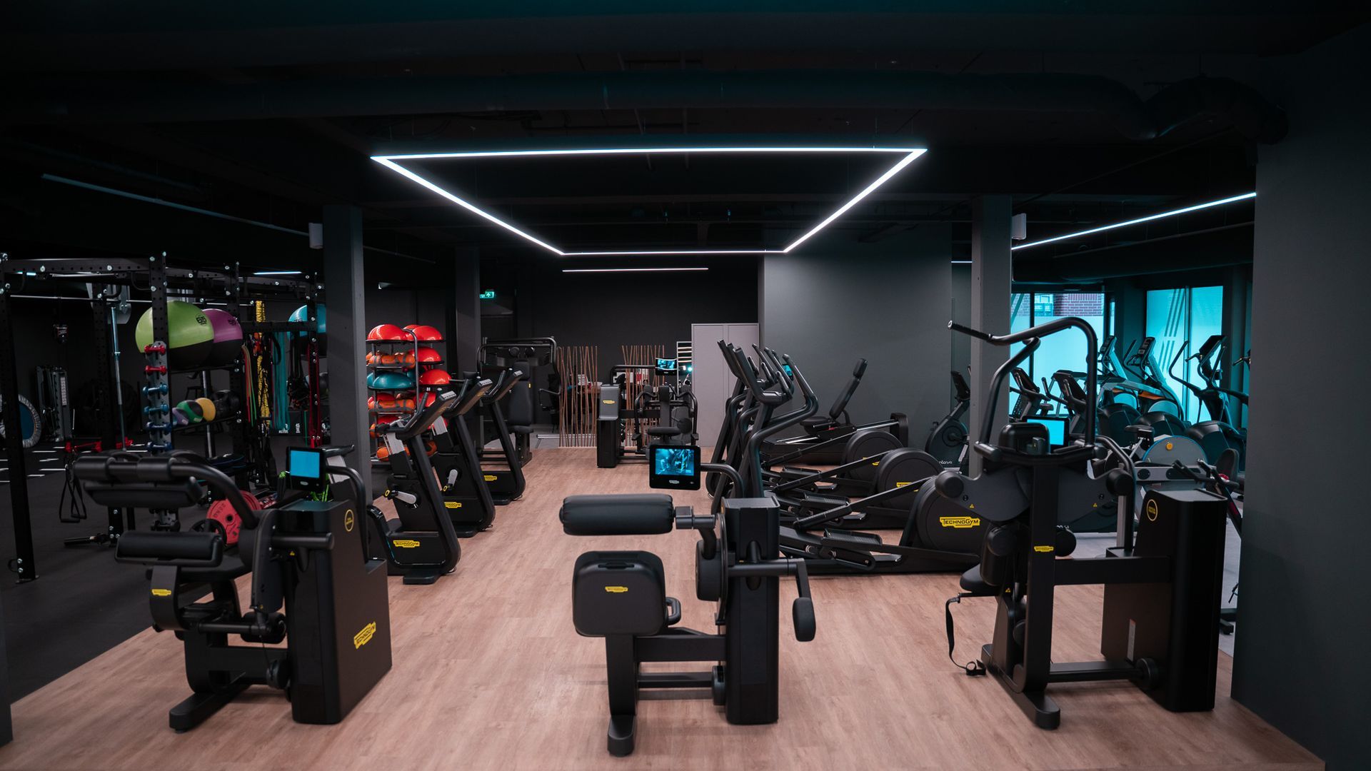 Interieur van een sportschool met diverse fitnessapparaten, een zwart-gele kleurstelling en tl-verlichting.