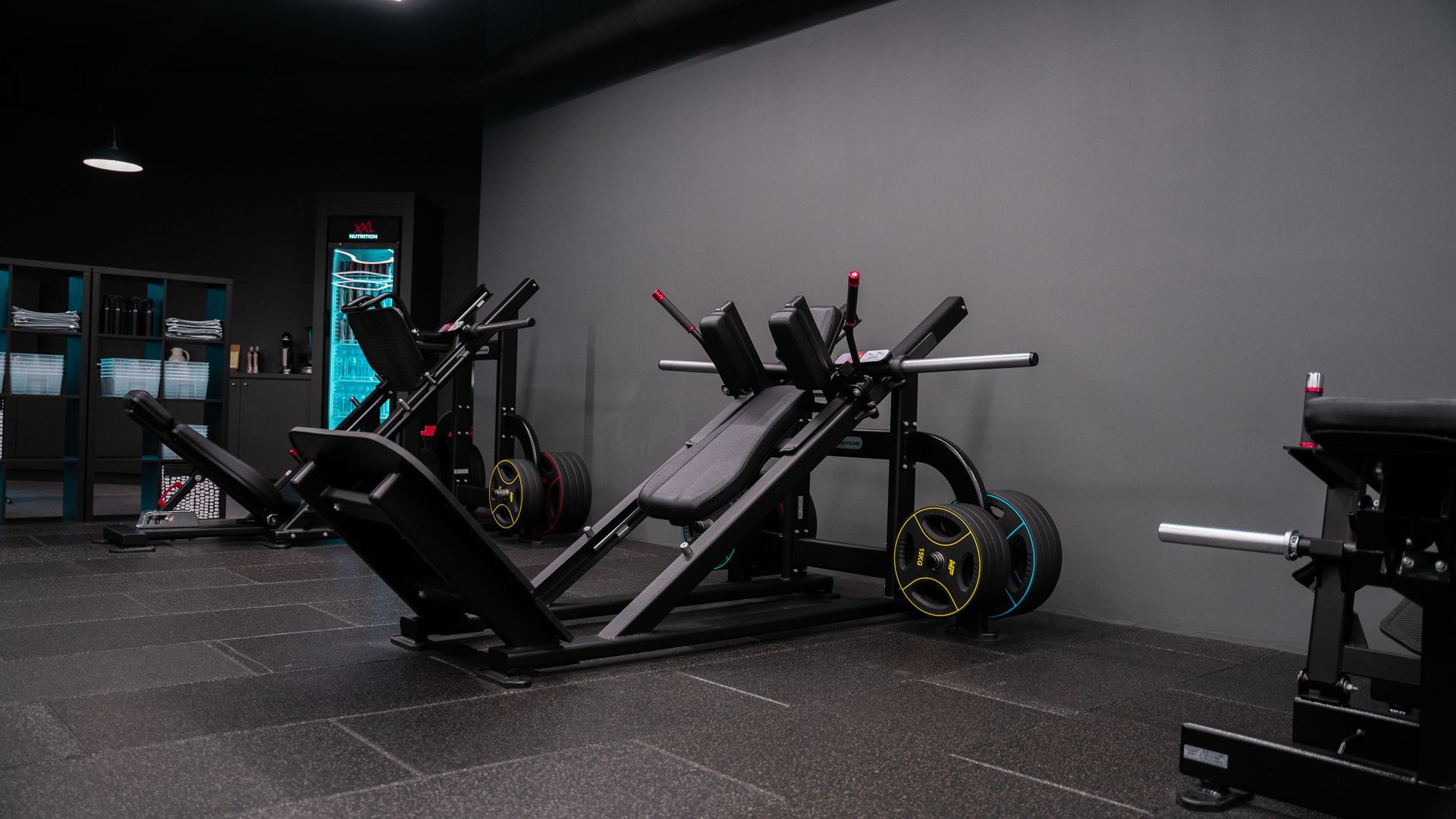 Interieur van een sportschool met een leg press-apparaat, zwarte vloer en grijze muren.