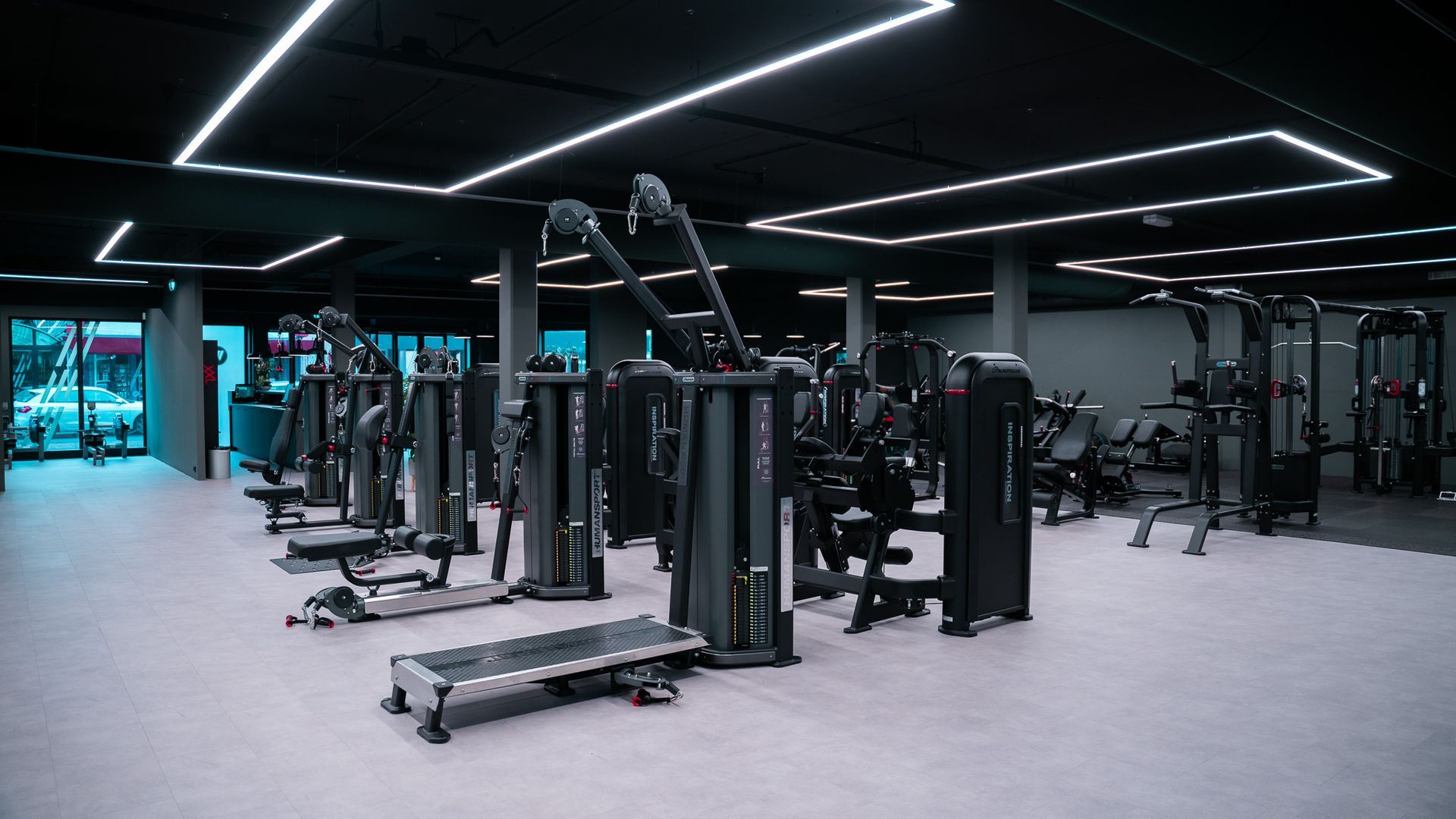 Een moderne sportschool met rijen fitnessapparaten, waaronder optrek- en kabelstations, onder heldere rechthoekige lampen.
