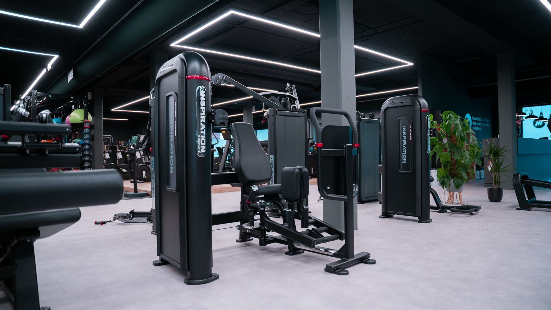 Interieur van een sportschool met zwarte fitnessapparaten, een grijze vloer en een zwart plafond met witte verlichting.