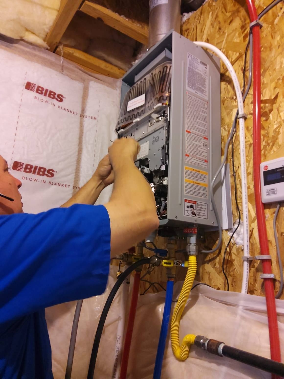 Electrician working on an open wall-mounted breaker panel in an unfinished wall space.