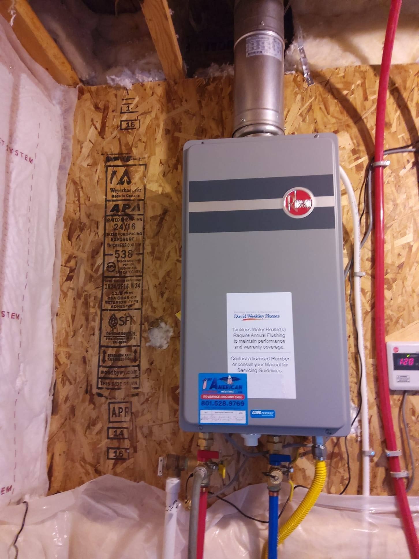 Residential furnace installed in a utility closet with exposed insulation and red and yellow pipes.