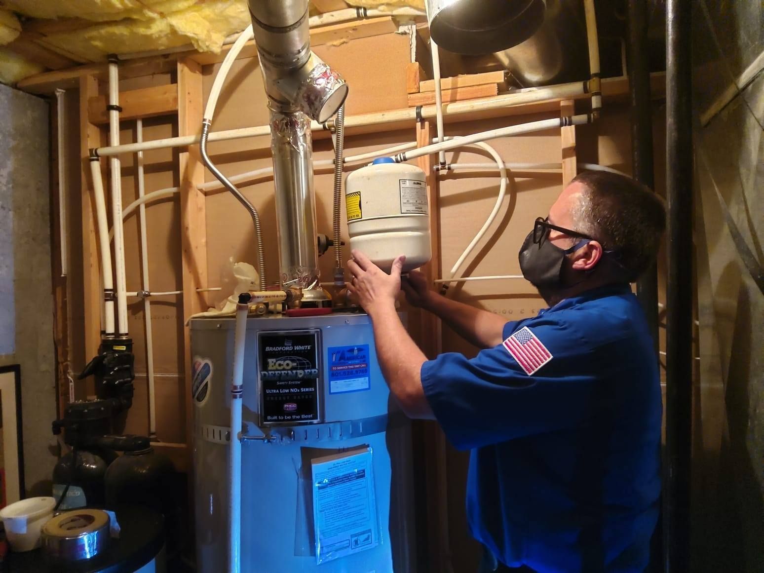 Technician in a basement inspecting a water heater and pipes with a flashlight and tools