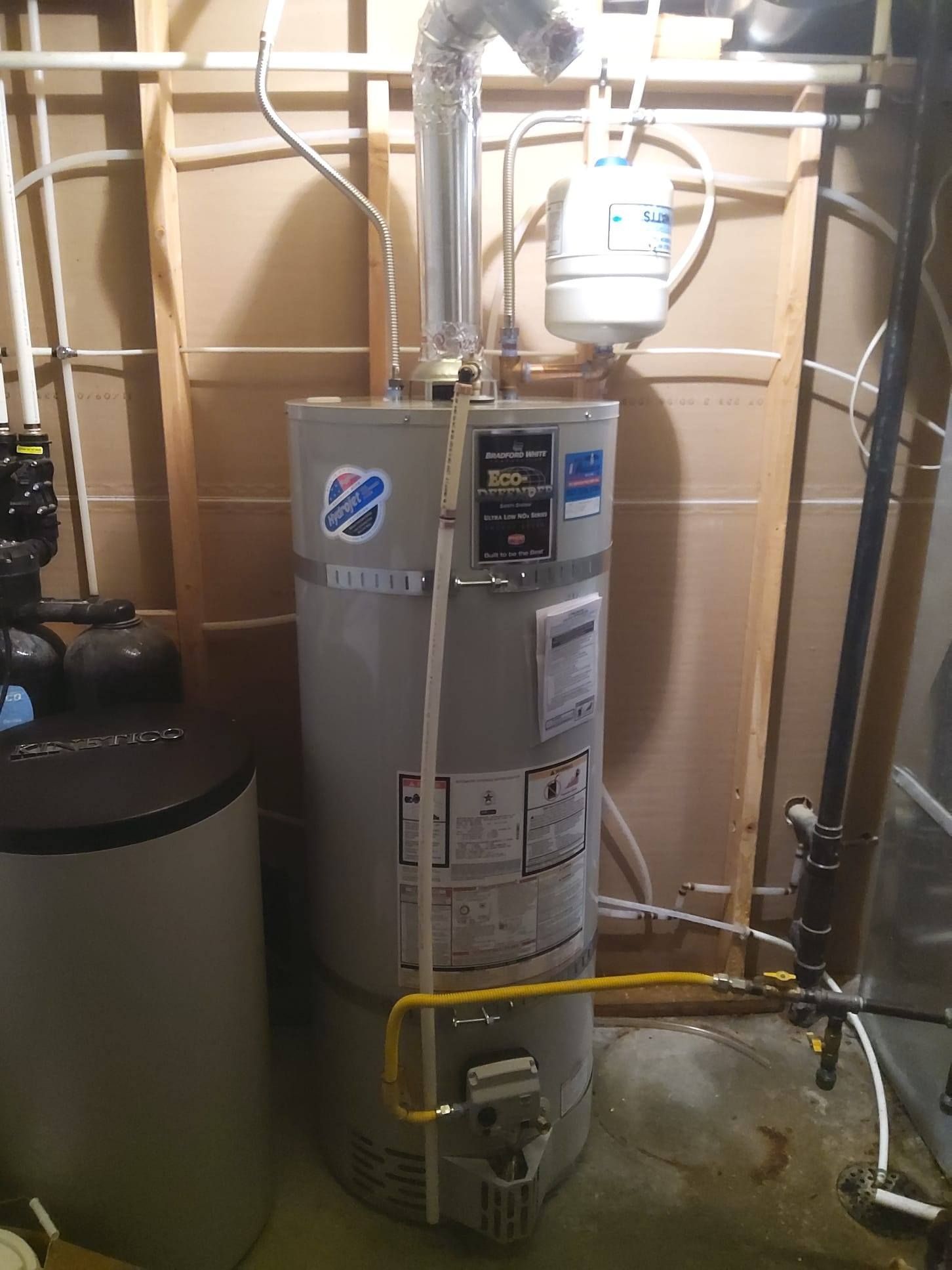 Water heater in a utility closet with pipes, valves, and a yellow gas line.