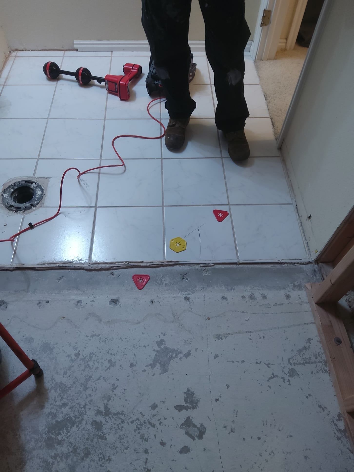 Person standing in a tiled room near a red drill and scattered markers on the floor