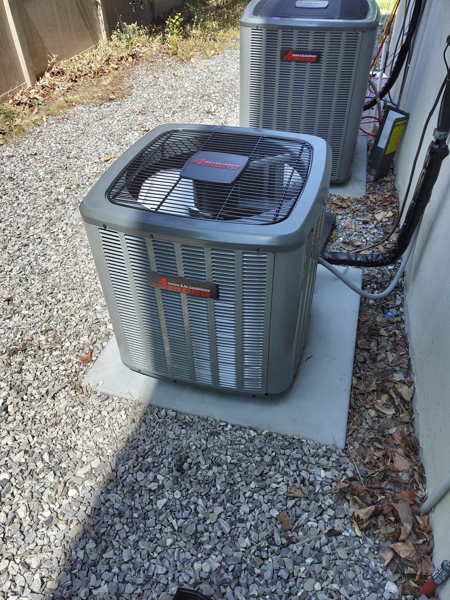 Outdoor air conditioner units on gravel beside a house, with leaves and debris nearby.