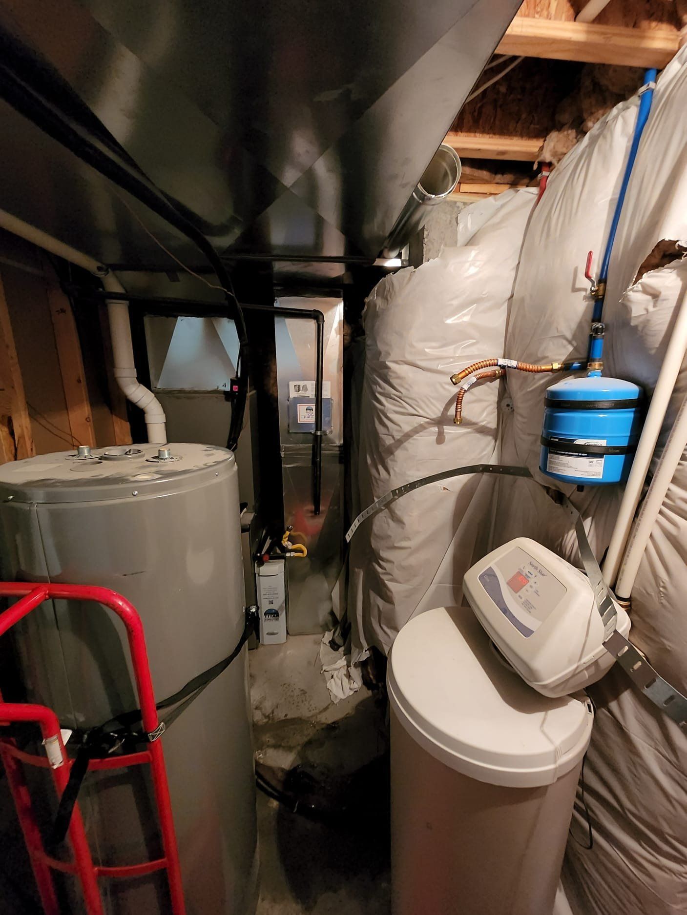 Basement utility area with water heater, furnace, filtration tank, and storage bins under exposed beams