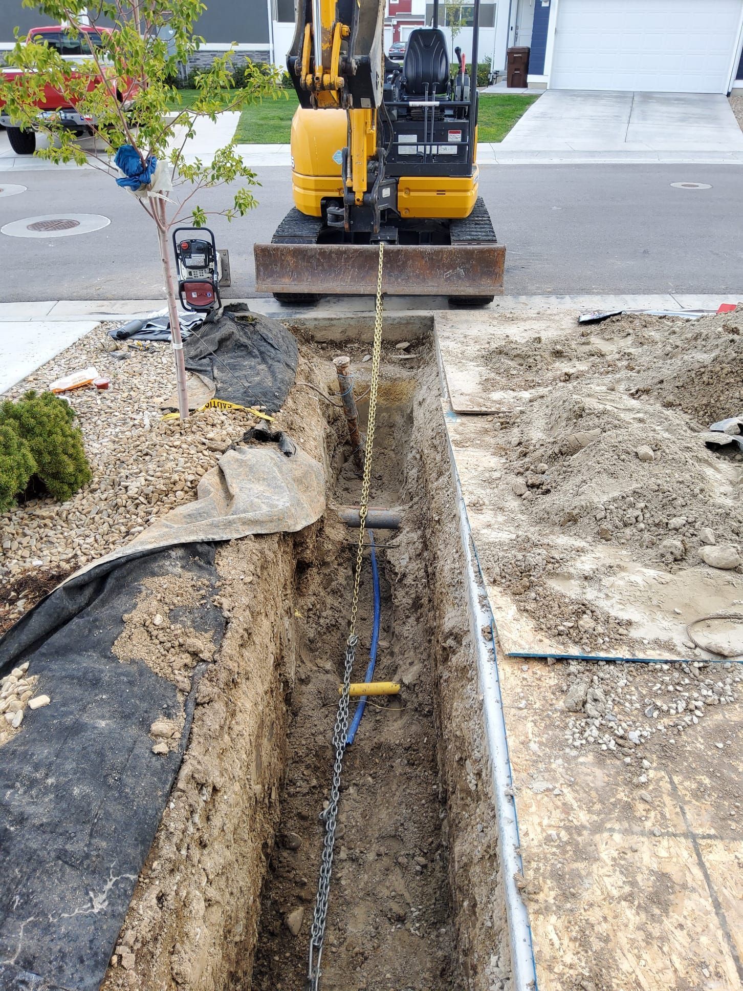 Backhoe digging a narrow trench beside a road, exposing underground utility lines.