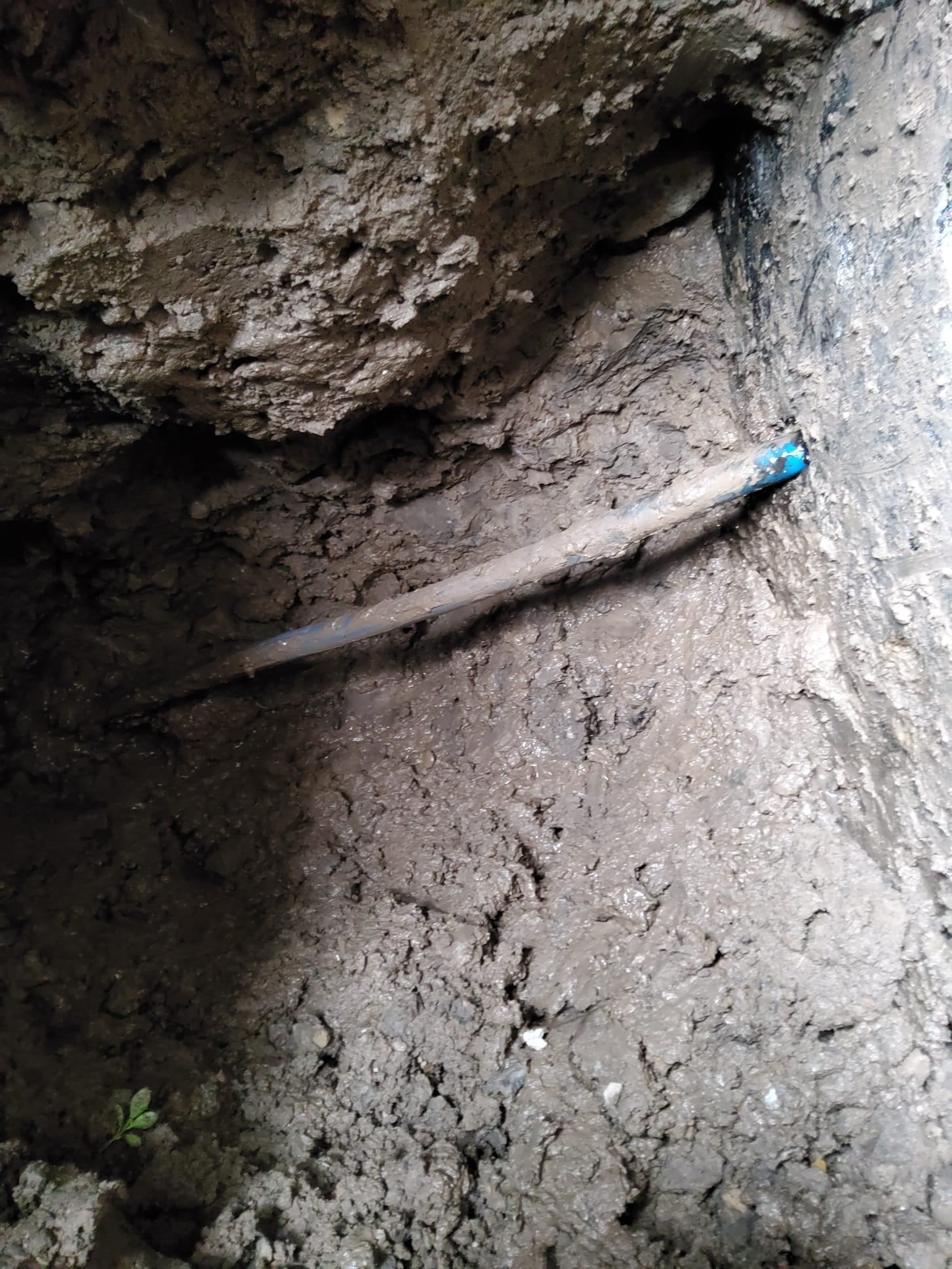 A muddy trench with a long pipe or rod running diagonally, ending in a blue cap.