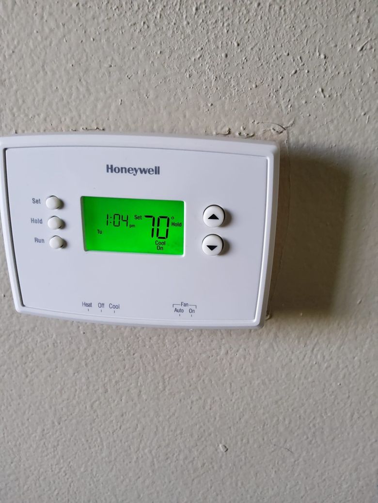 Honeywell wall thermostat with green digital display on a beige wall