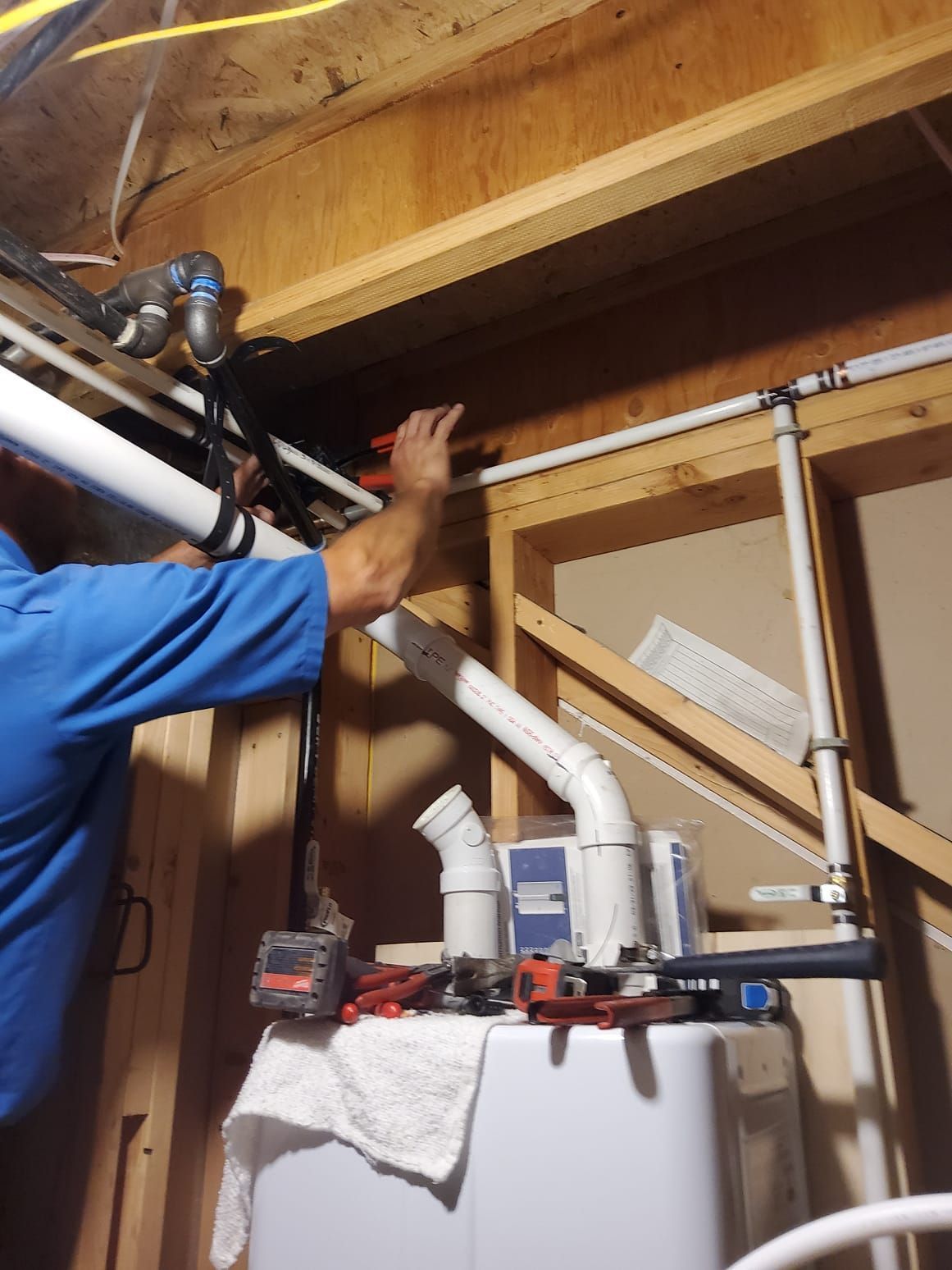 Person working on pipes above a water heater in an unfinished basement