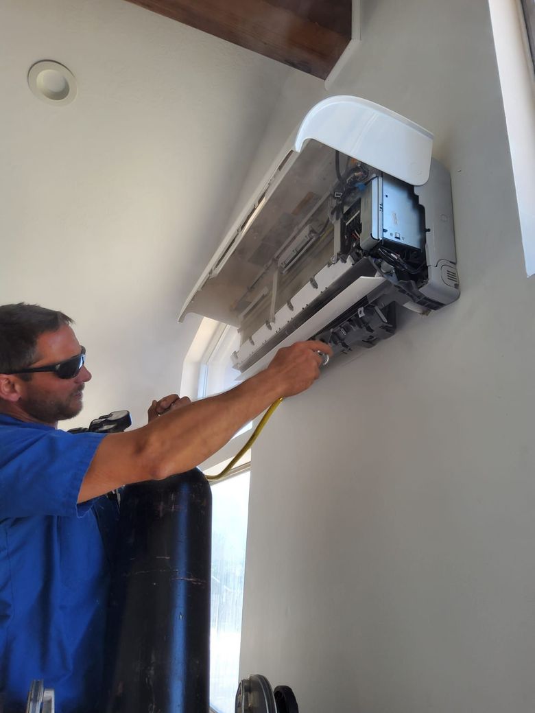 Technician in blue shirt servicing a wall-mounted air conditioner indoors.