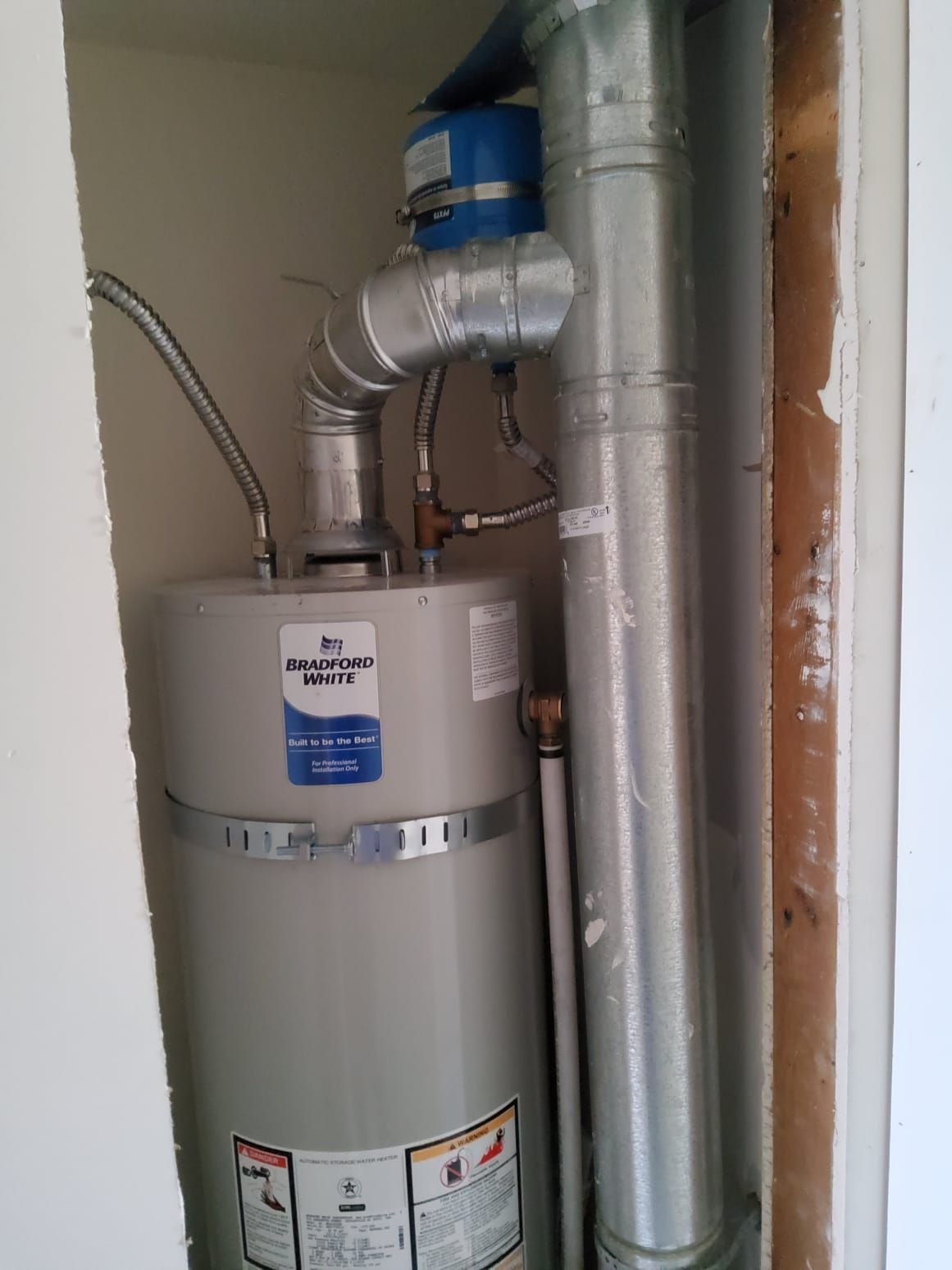 Water heater with silver ductwork and blue vent pipe in a utility closet