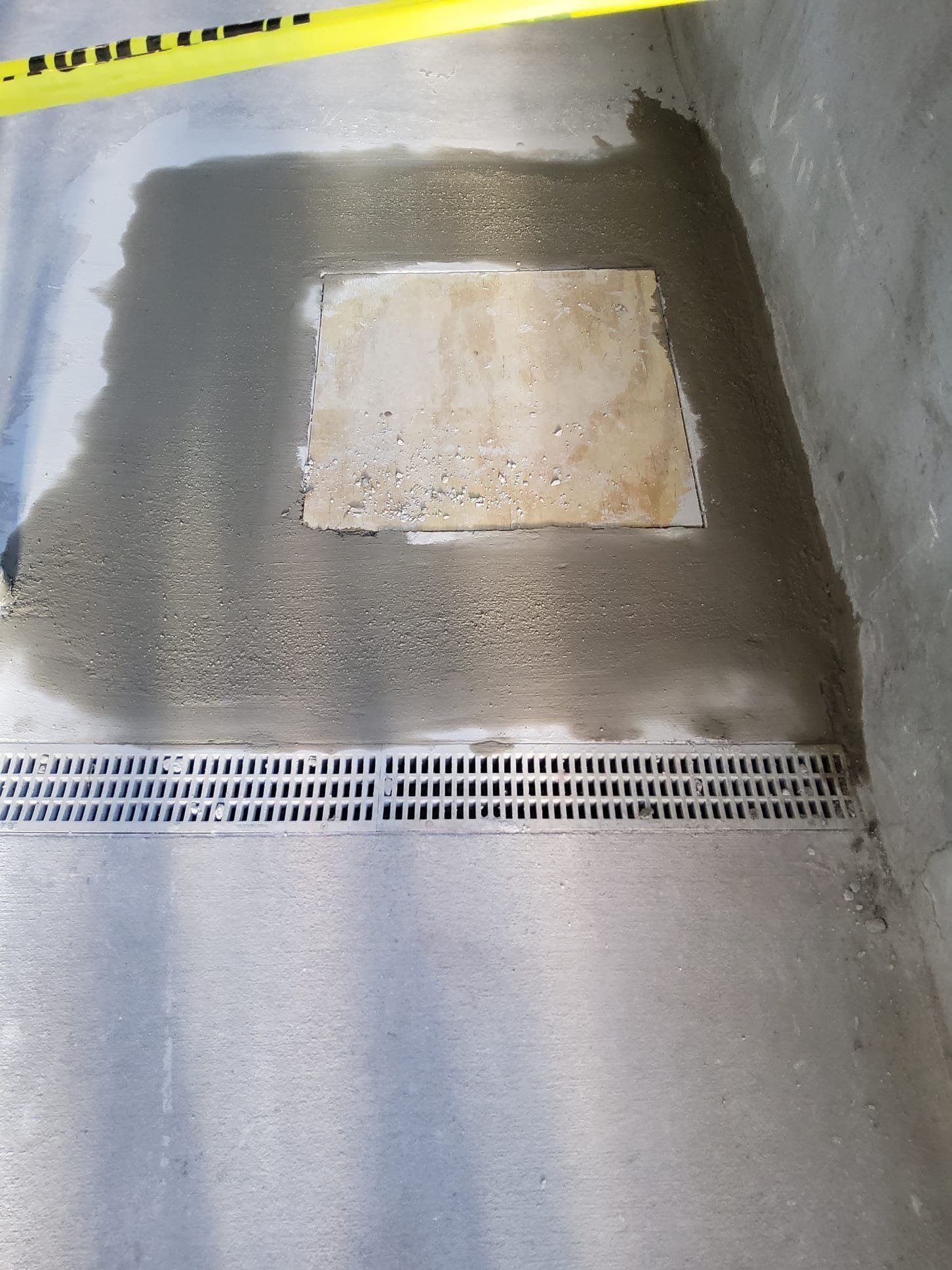 Concrete floor with a repaired patch and drainage grate, viewed from above.