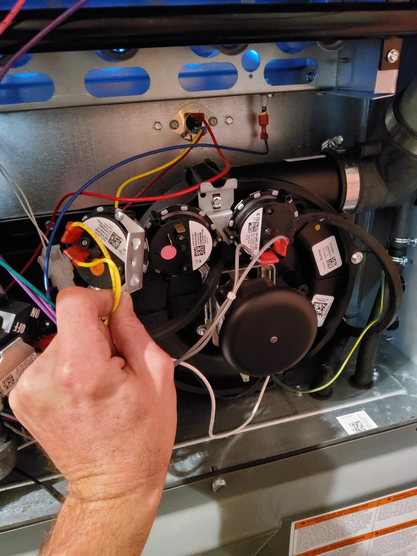 Technician hand adjusting wires inside a furnace’s open control compartment
