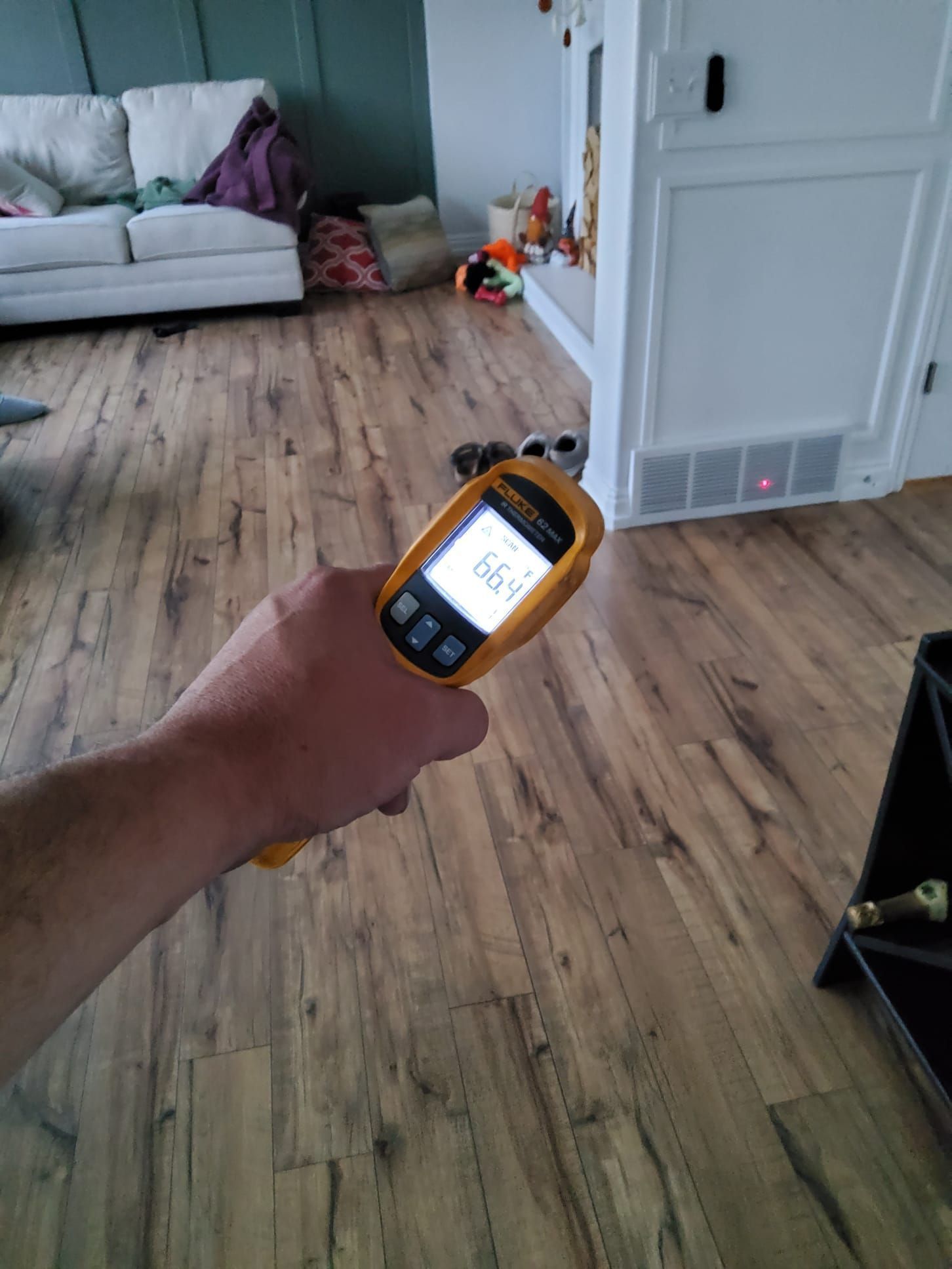 Hand holding a yellow laser measurer over a wood floor in a living room