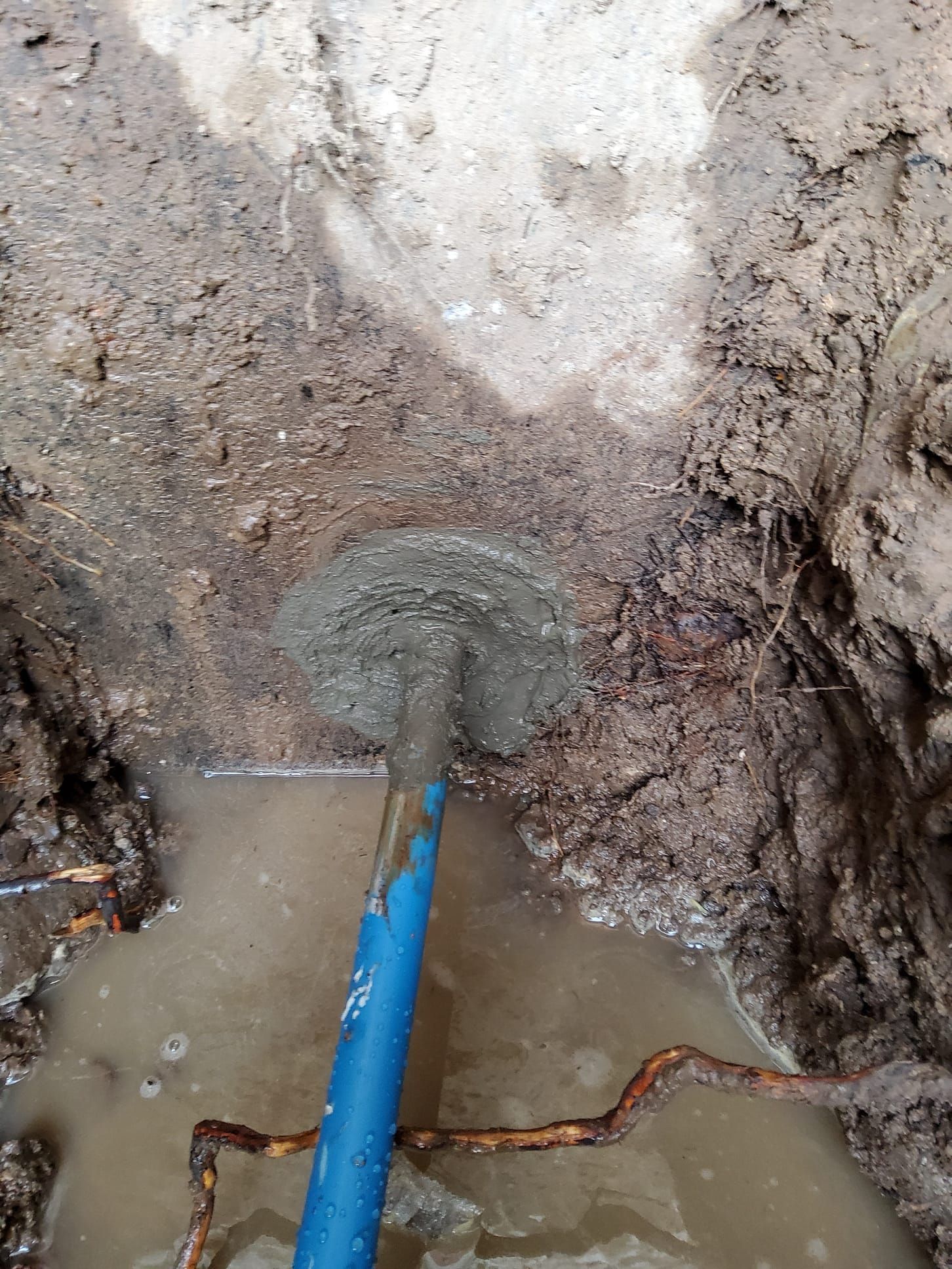 Blue pipe entering muddy excavation wall with water pooling at the bottom