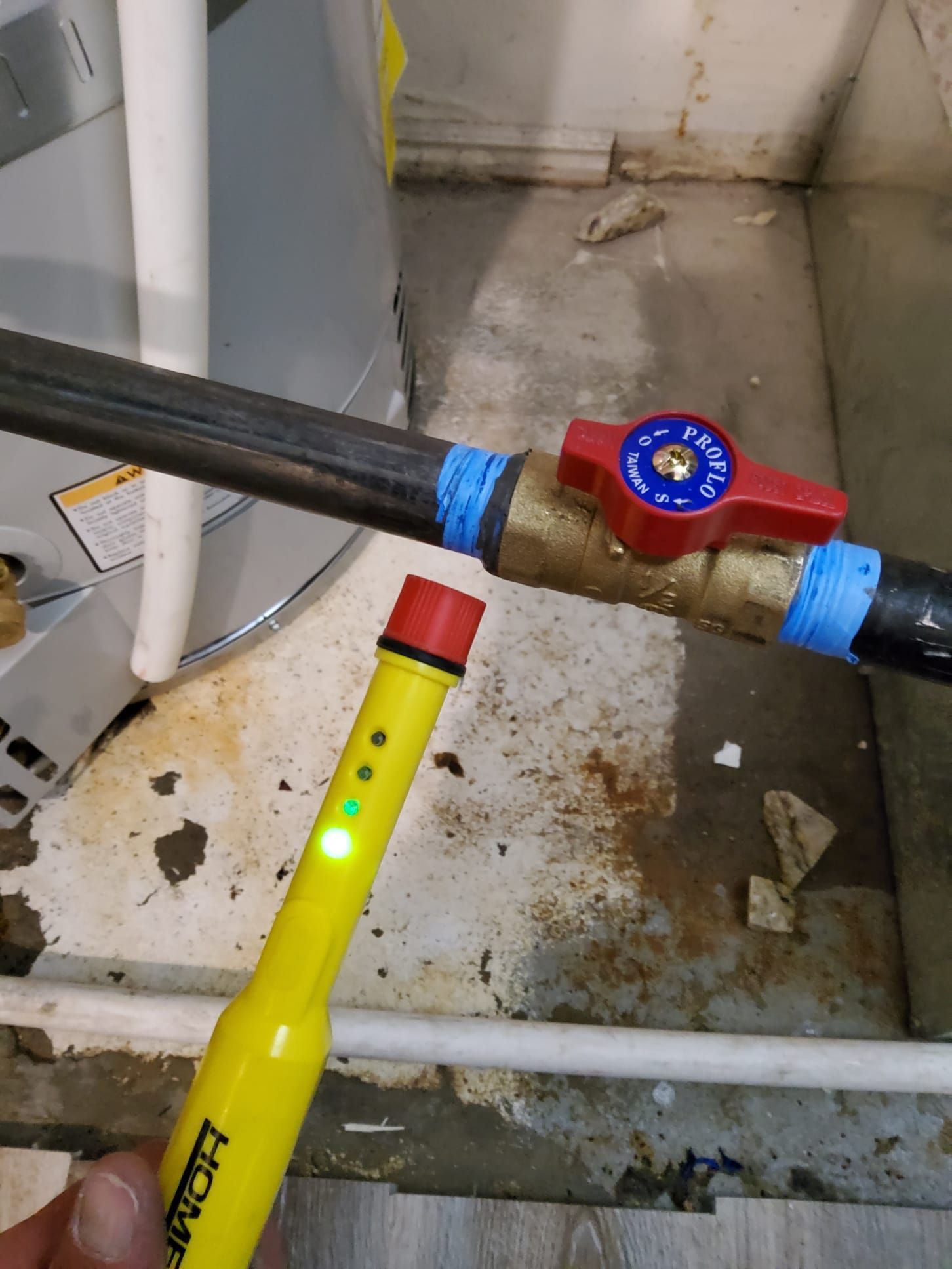 Yellow wand testing a black pipe valve with a red handle in a utility room