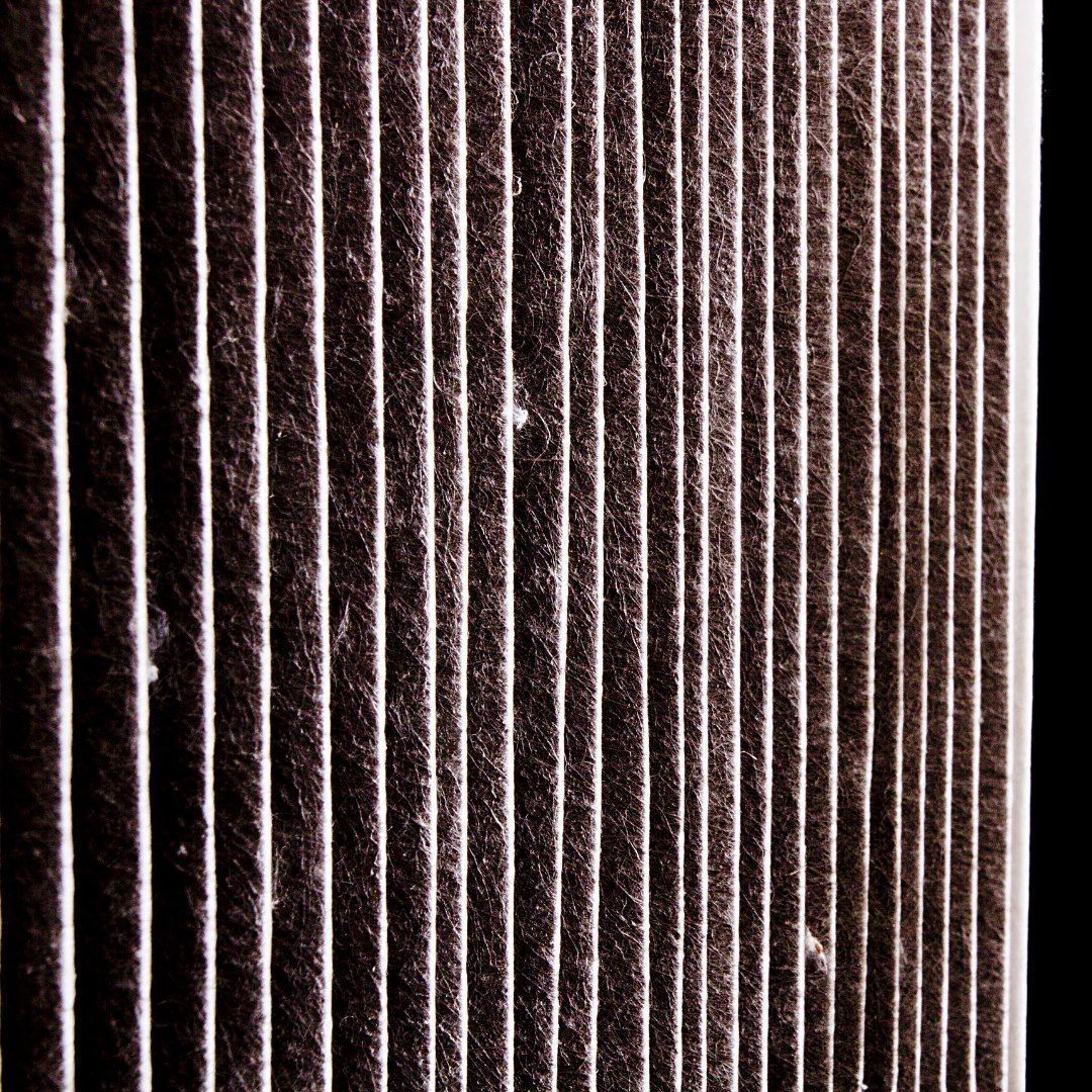 Close-up of a brown pleated air filter with vertical ridges and white dust specks