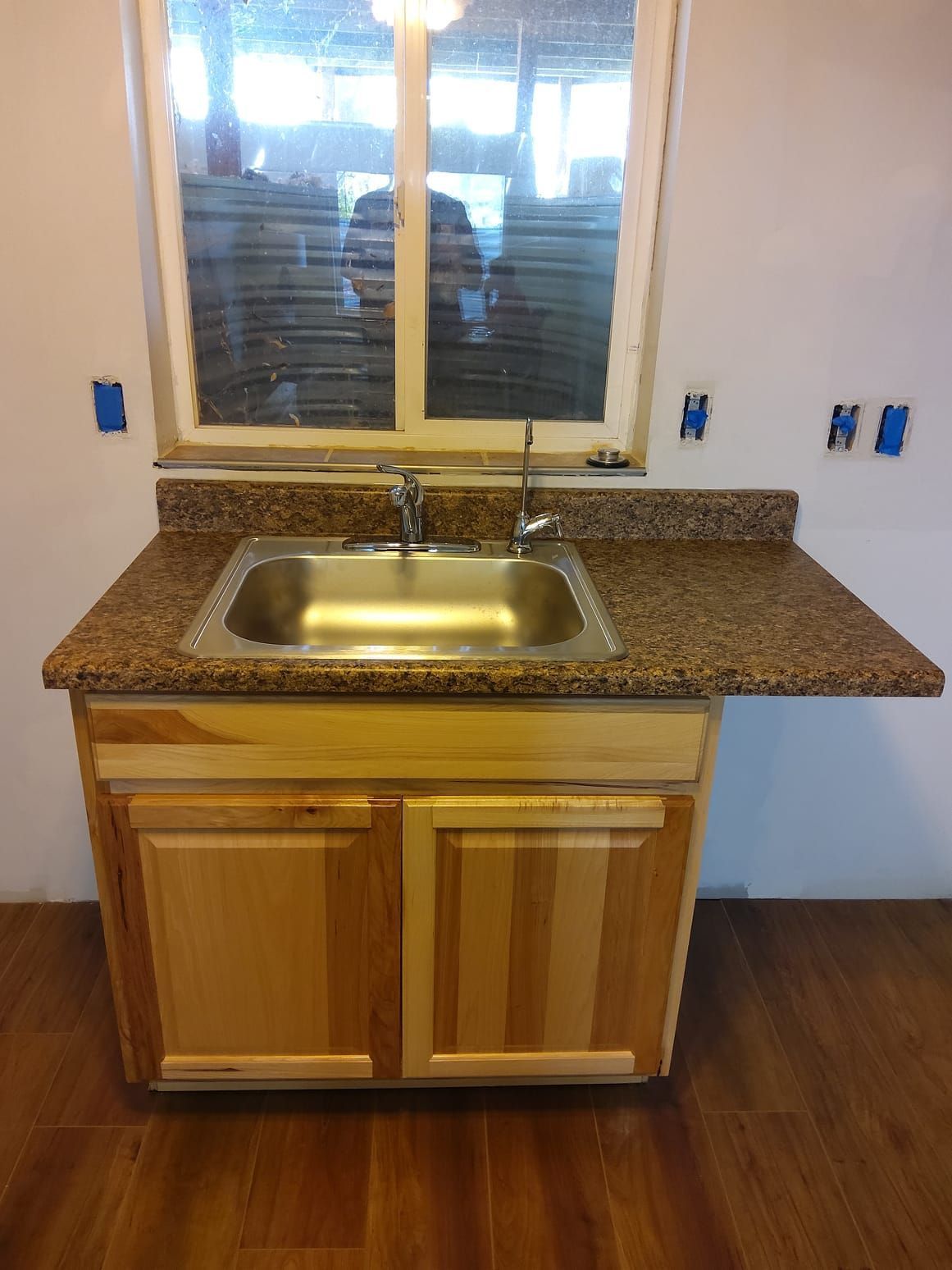 Wooden kitchen sink cabinet with speckled granite countertop under a window, in a newly renovated room