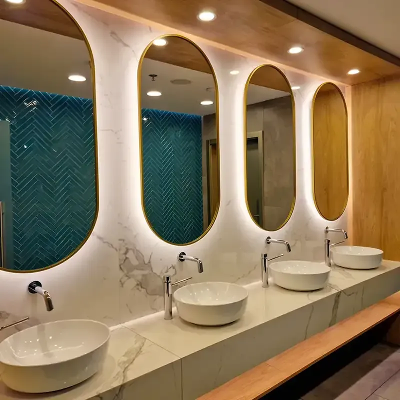 Modern restroom with four oval mirrors, white sinks, marble countertop, and wood-and-teal decor