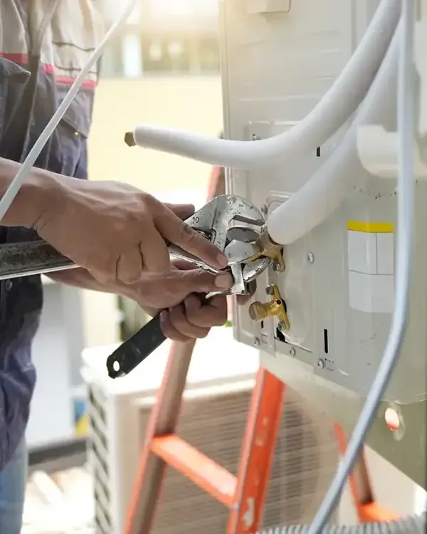 Technician using a tool to repair white outdoor HVAC unit