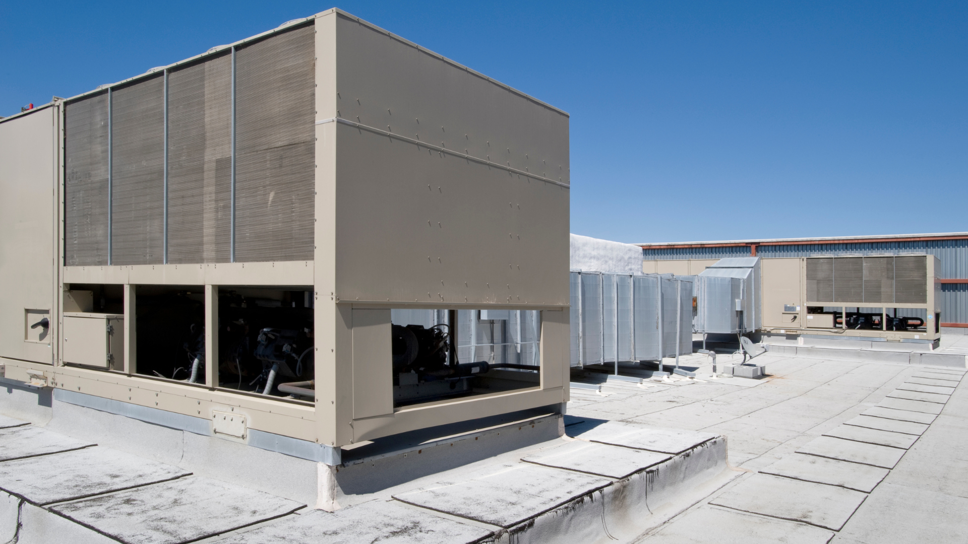 Rooftop view of large HVAC units and beige utility buildings under a clear blue sky.