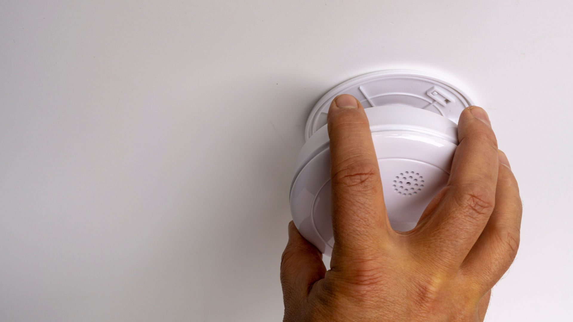Hand installing a white smoke detector on a ceiling.