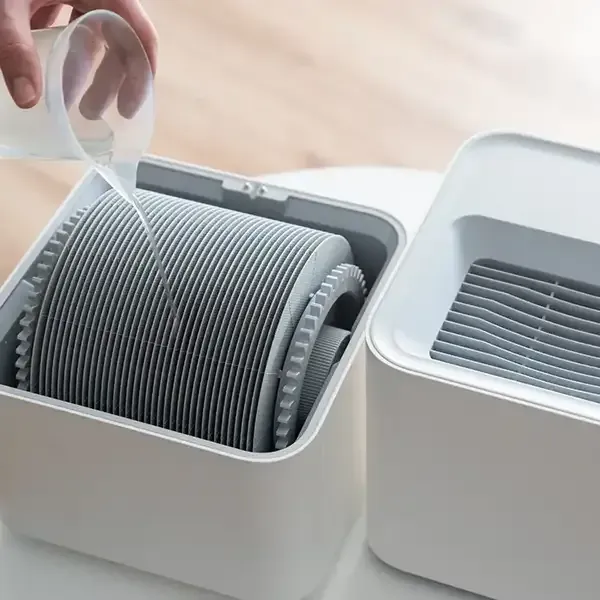 Hand placing a filter into a white air purifier on a wooden table, with another purifier beside it