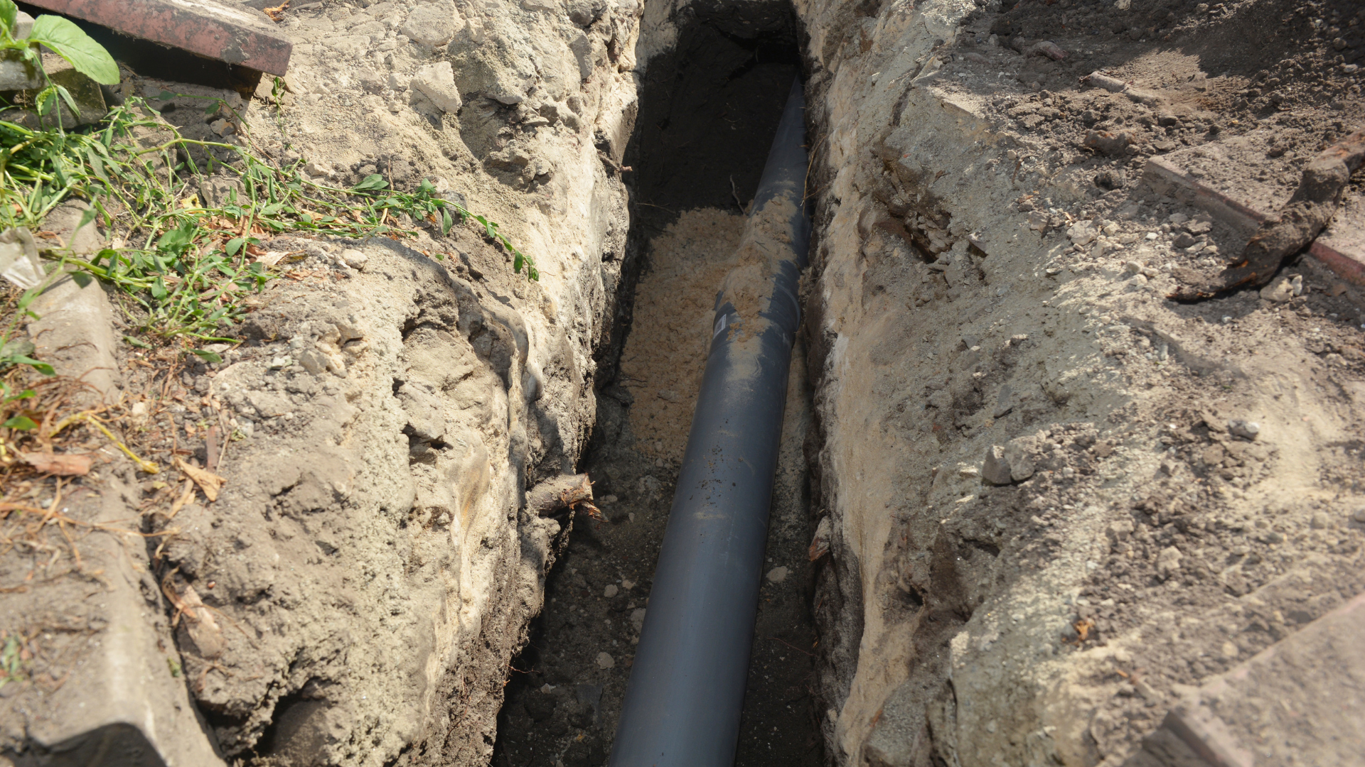Black pipe laid in a narrow dirt trench between exposed soil walls.