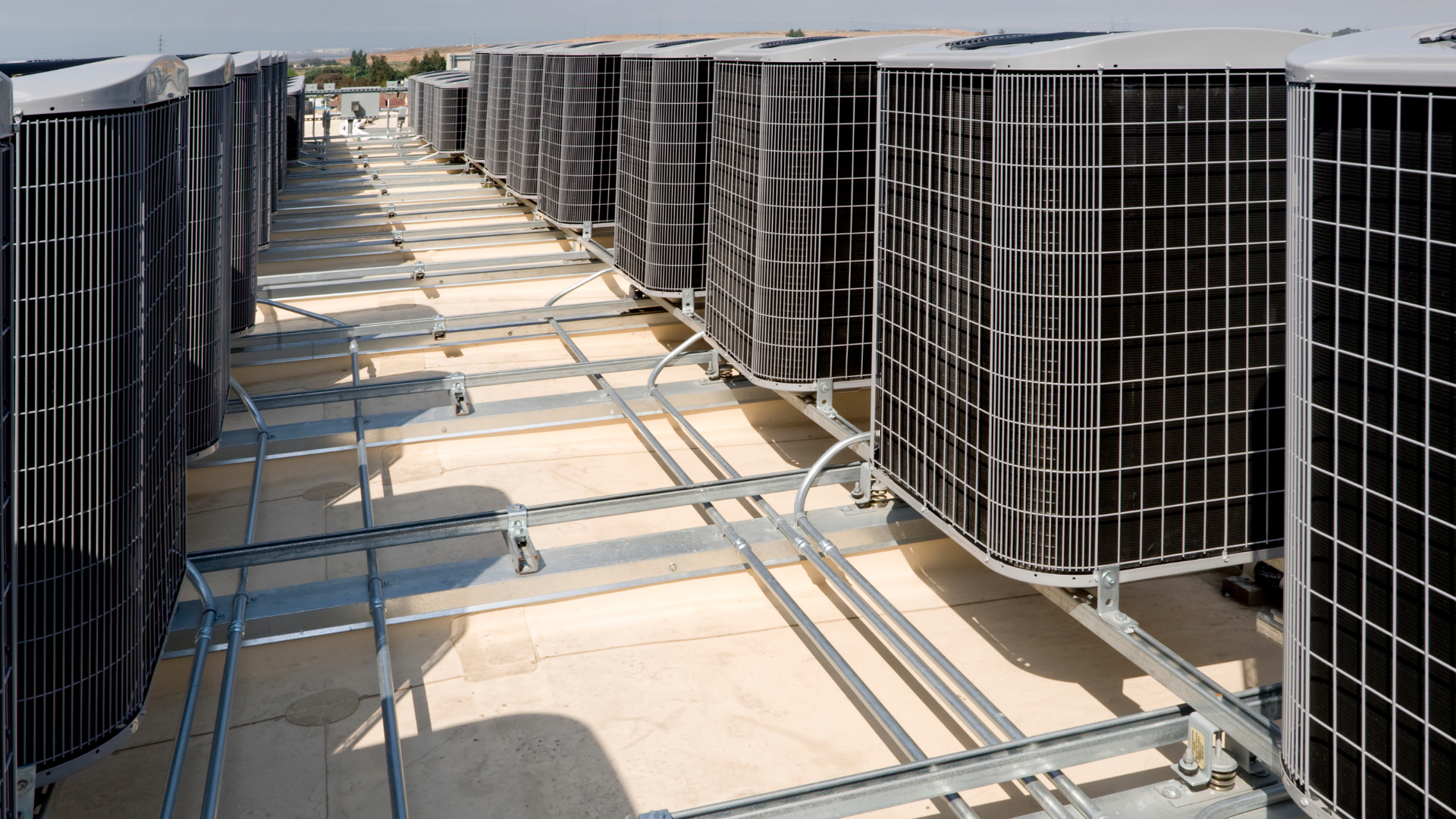 Rows of rooftop HVAC units with metal grates and ducts on a flat roof