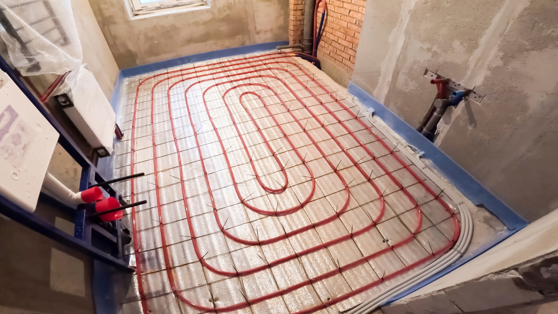 Underfloor heating pipes laid in a room under construction, with red tubing over insulation panels.