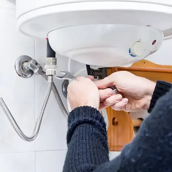 Plumber tightening pipes under a white sink with a wrench in a tiled bathroom