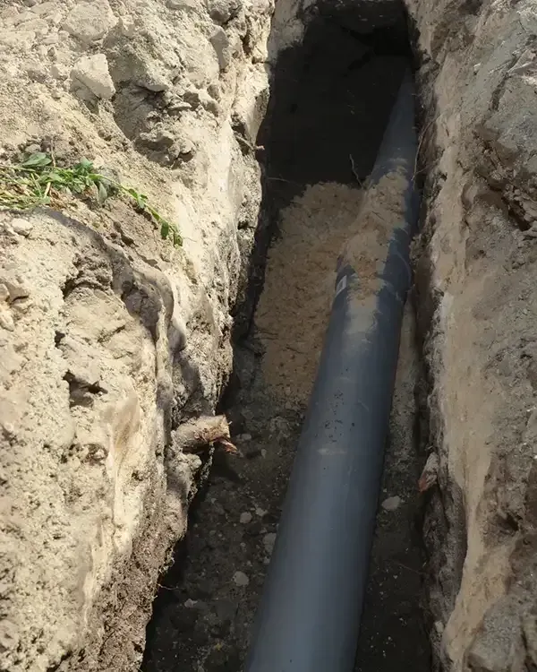 Black pipe laid in a narrow dirt trench between exposed soil walls.