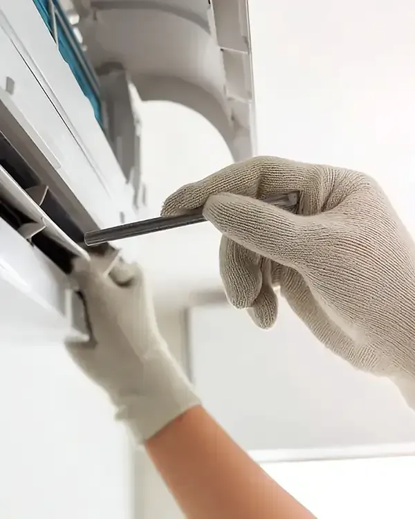 Gloved hands using a screwdriver to repair a white wall-mounted air conditioner unit