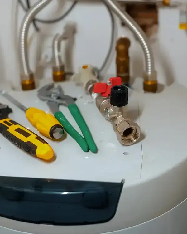 Tools on top of a white water heater with pipes and valves behind it.