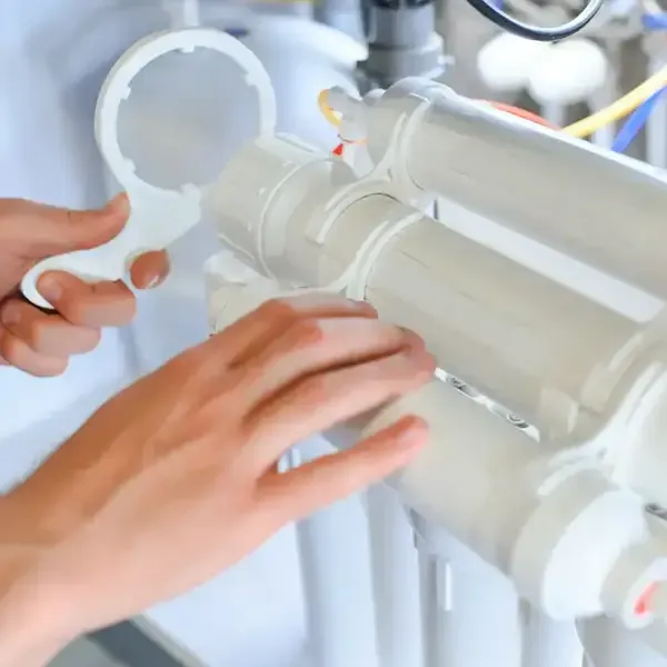 Hands adjusting a white industrial filter cartridge assembly with pipes and colored tubes in a lab setting
