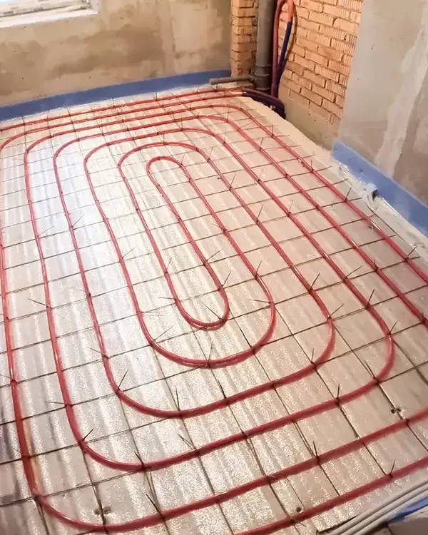 Underfloor heating pipes laid in a room under construction, with red tubing over insulation panels.