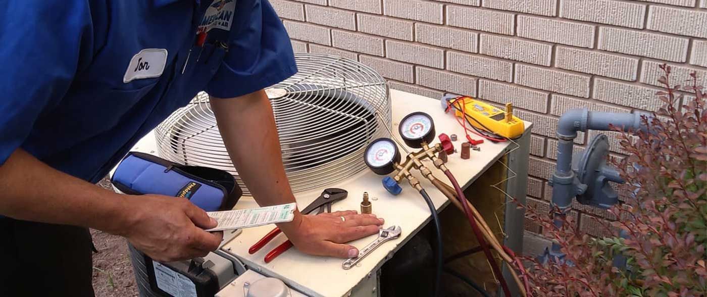 Hands connect a hose fitting between red and blue water valves under a sink