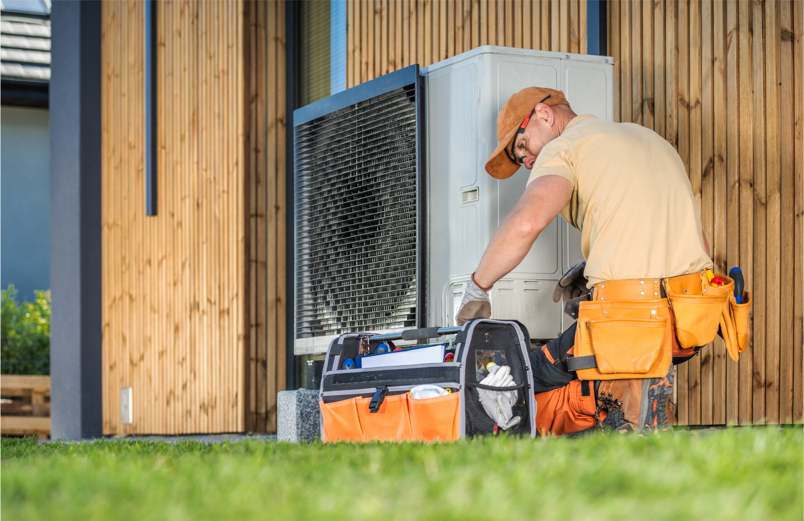 HVAC technician working on an outdoor air conditioning unit next to a wooden wall.