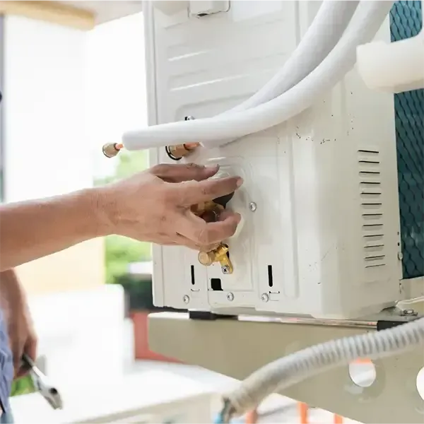 Technician repairing a white air conditioner unit outdoors with hoses attached