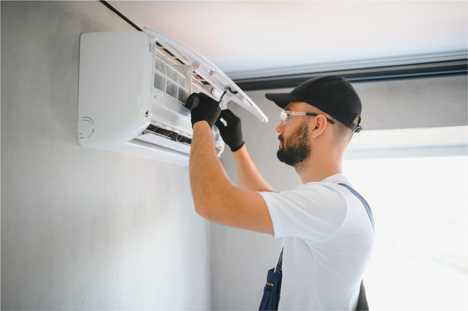 Technician repairing a wall-mounted air conditioner with tools in a bright room