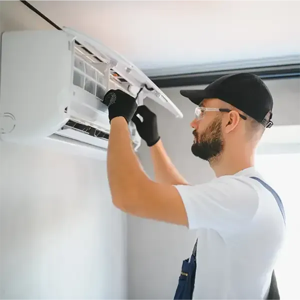 Technician repairing a wall-mounted air conditioner with tools in a bright room