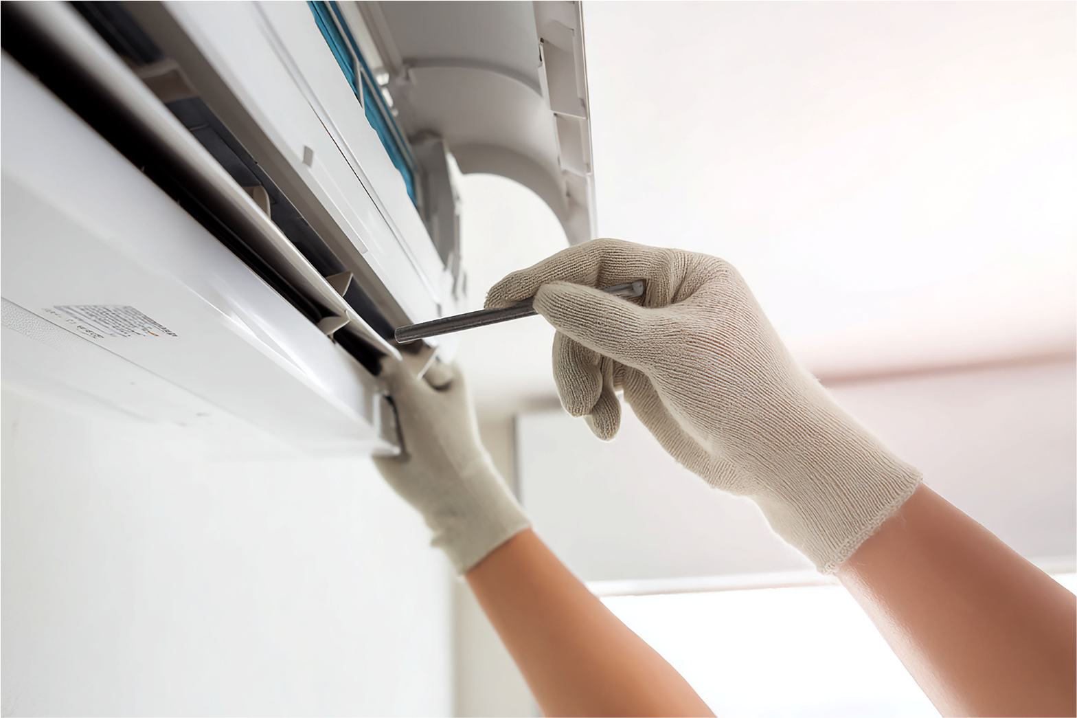 Gloved hands cleaning an air conditioner vent with a screwdriver and cloth