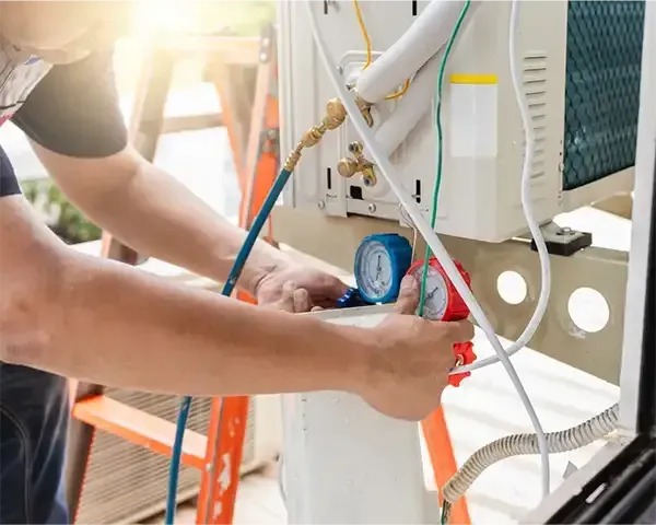 Technician connecting gauges to outdoor HVAC unit during maintenance