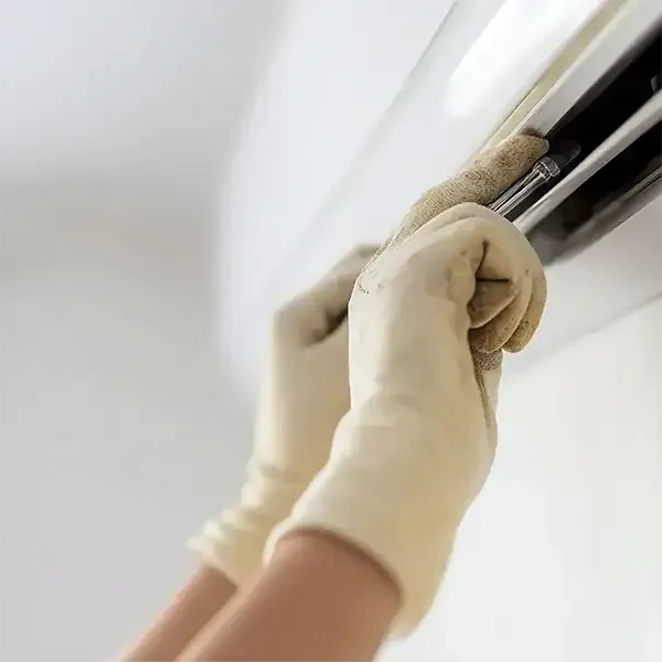 Gloved hands cleaning a wall-mounted air conditioner vent indoors