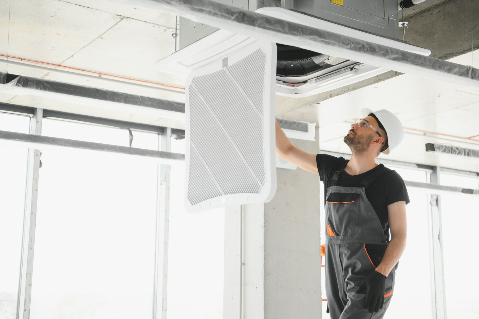 Worker installing a white ceiling vent in an unfinished room