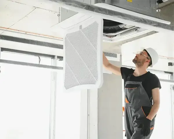 Worker installing a white ceiling vent in an unfinished room